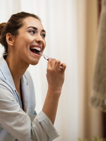 Mulher jovem escovando os dentes e se olhando no espelho