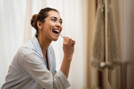 Mulher jovem escovando os dentes e se olhando no espelho