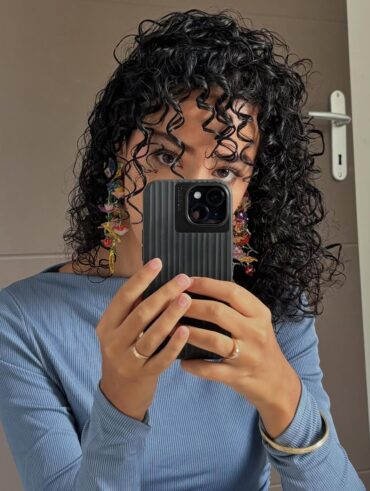 Mulher de pele clara, com blusa azul, brinco colorido e cabelo crespo preto
