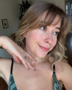 Mulher de pele clara, com regata, rosácea nas bochechas e cabelo loiro