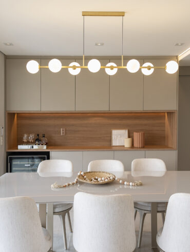 Sala de jantar com mesa retangular clara, cadeiras estofadas, e pendente com esferas