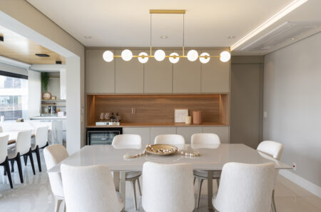 Sala de jantar com mesa retangular clara, cadeiras estofadas, e pendente com esferas