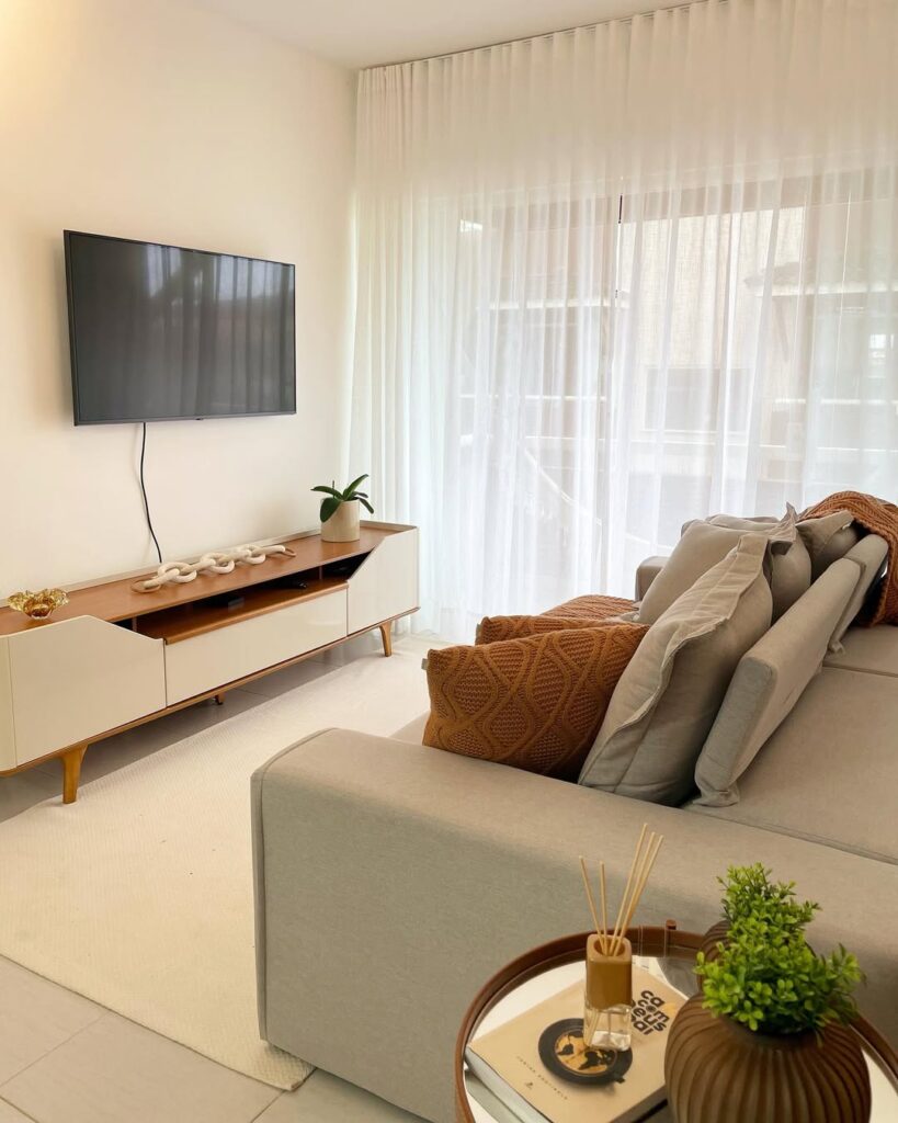 Sala de estar aconchegante com sofá, TV, rack, tapete e cortina branca