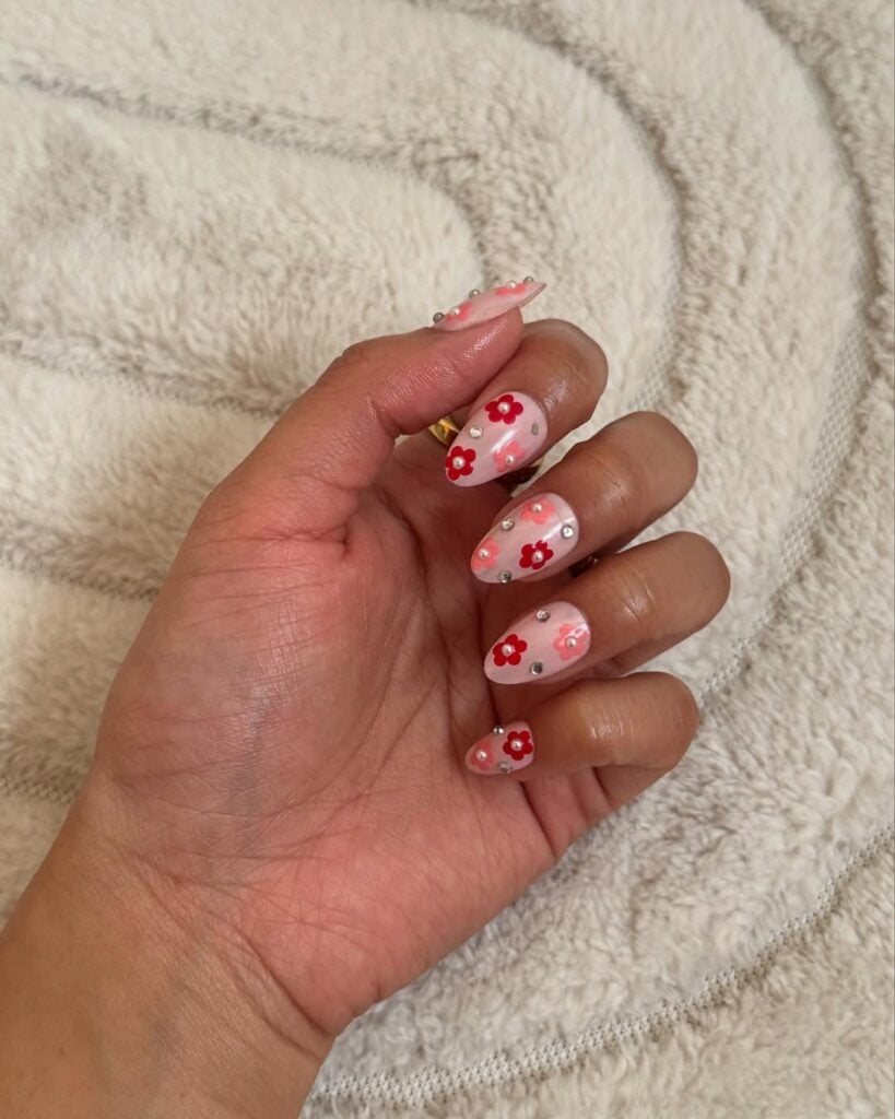 Mão de pele clara, com unha amendoada nude com flores em rosa e strass