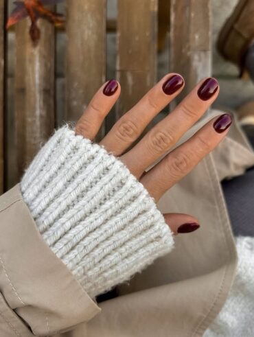 Mão de pele clara, com unha curta e arredondada burgundy
