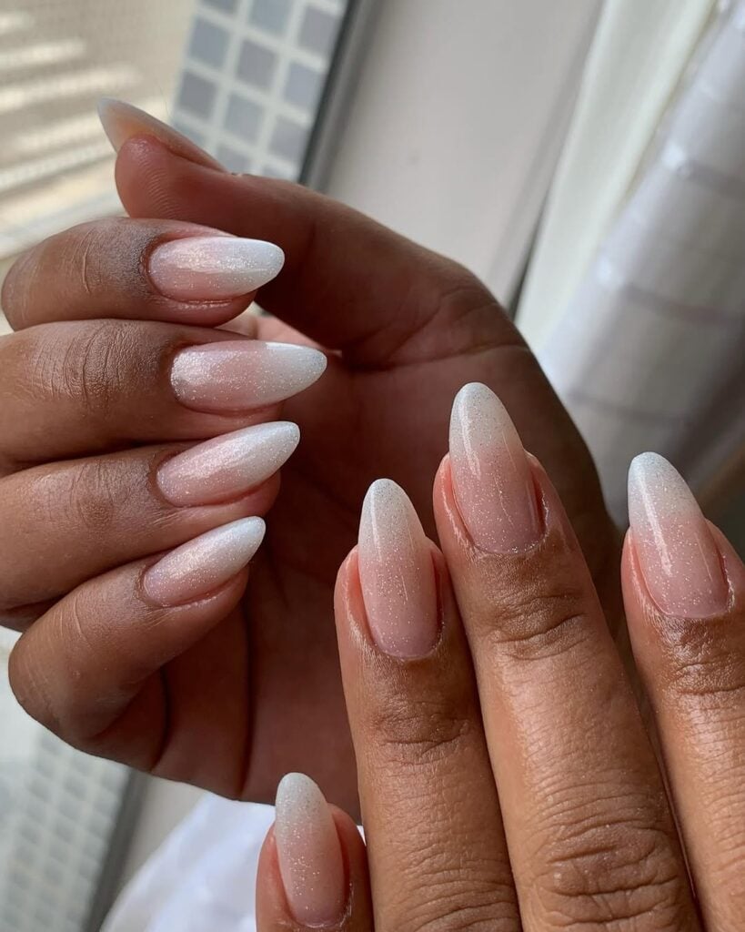 Mãos de pele preta, com unha amendoada baby boomer, finalizada com top coat de brilho