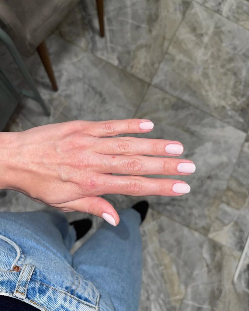 Mão de pele clara, com unha curta e arredondada pintada com esmalte rosa-claro
