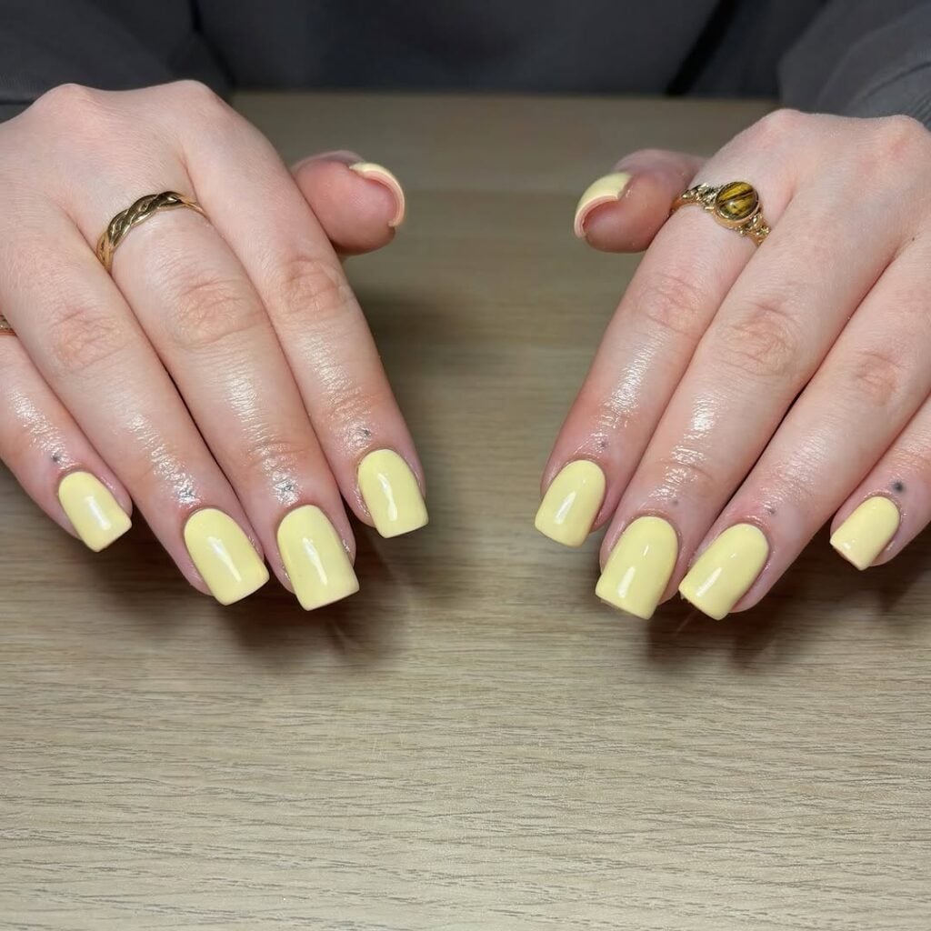 Mãos de pele clara, com anéis em dourado e unha squoval amarelo-manteiga