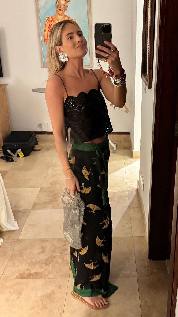 Mulher jovem em foto na frente do espelho. Ela usa calça, regata e rasteirinha.