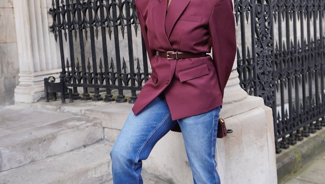 Mulher jovem e magra com blazer burgundy e calça jeans.