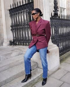 Mulher jovem e magra com blazer burgundy e calça jeans.