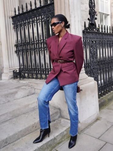 Mulher jovem e magra com blazer burgundy e calça jeans.