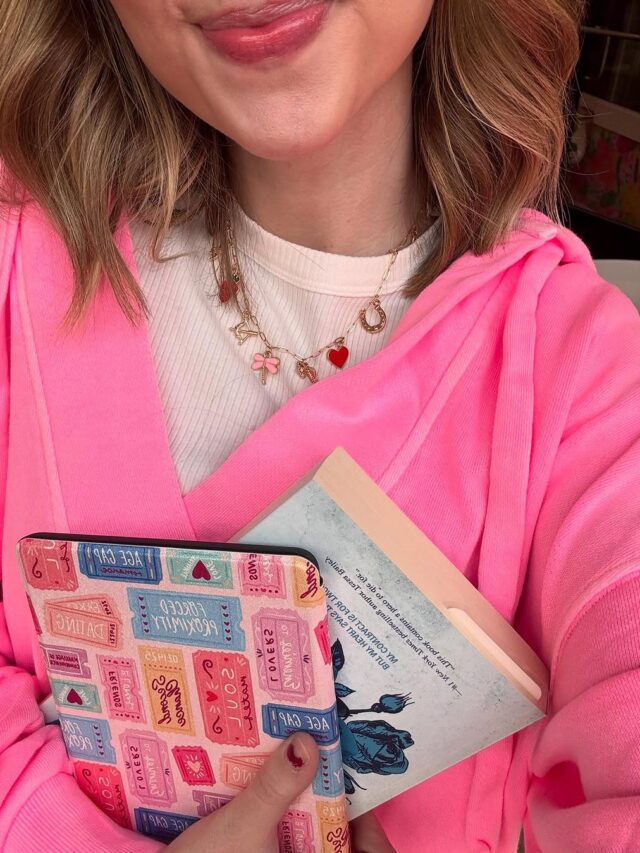 Mulher de pele clara, com blusa branca, casaco rosa e acessório colorido. Ela está segurando um Kindle e um livro