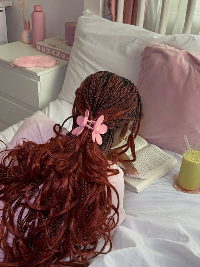 Mulher jovem deitada de bruços na cama lendo um livro