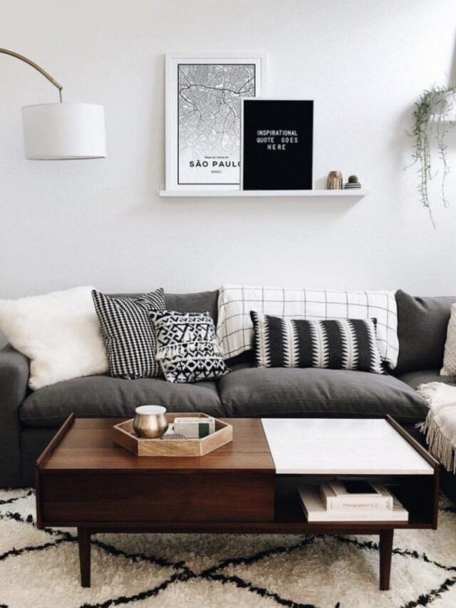 Sala com sofá cinza escuro, almofadas em branco e preto, e quadros na prateleira na parede