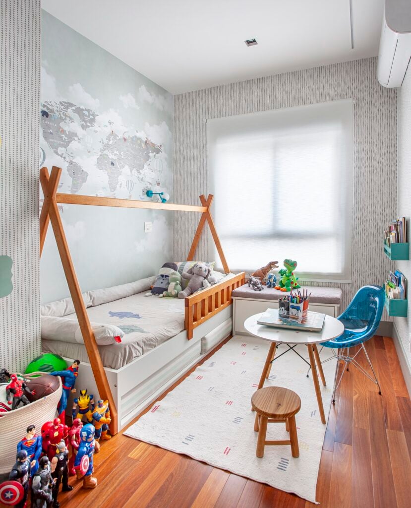 Quarto de criança com mapaz mundi na parede lateral à cama, mesa e cadeira e bonecos de super-heróis