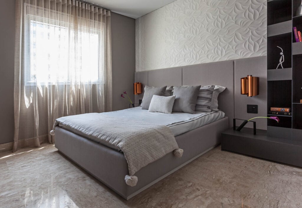 Quarto de casal com cama e cabeceira cinza e meia parede em gesso