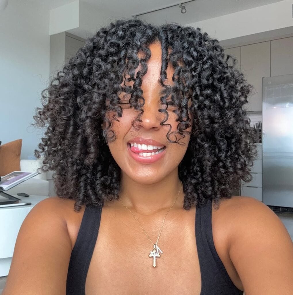Mulher negra com cabelo curto, no estilo bob com franja e cacheado