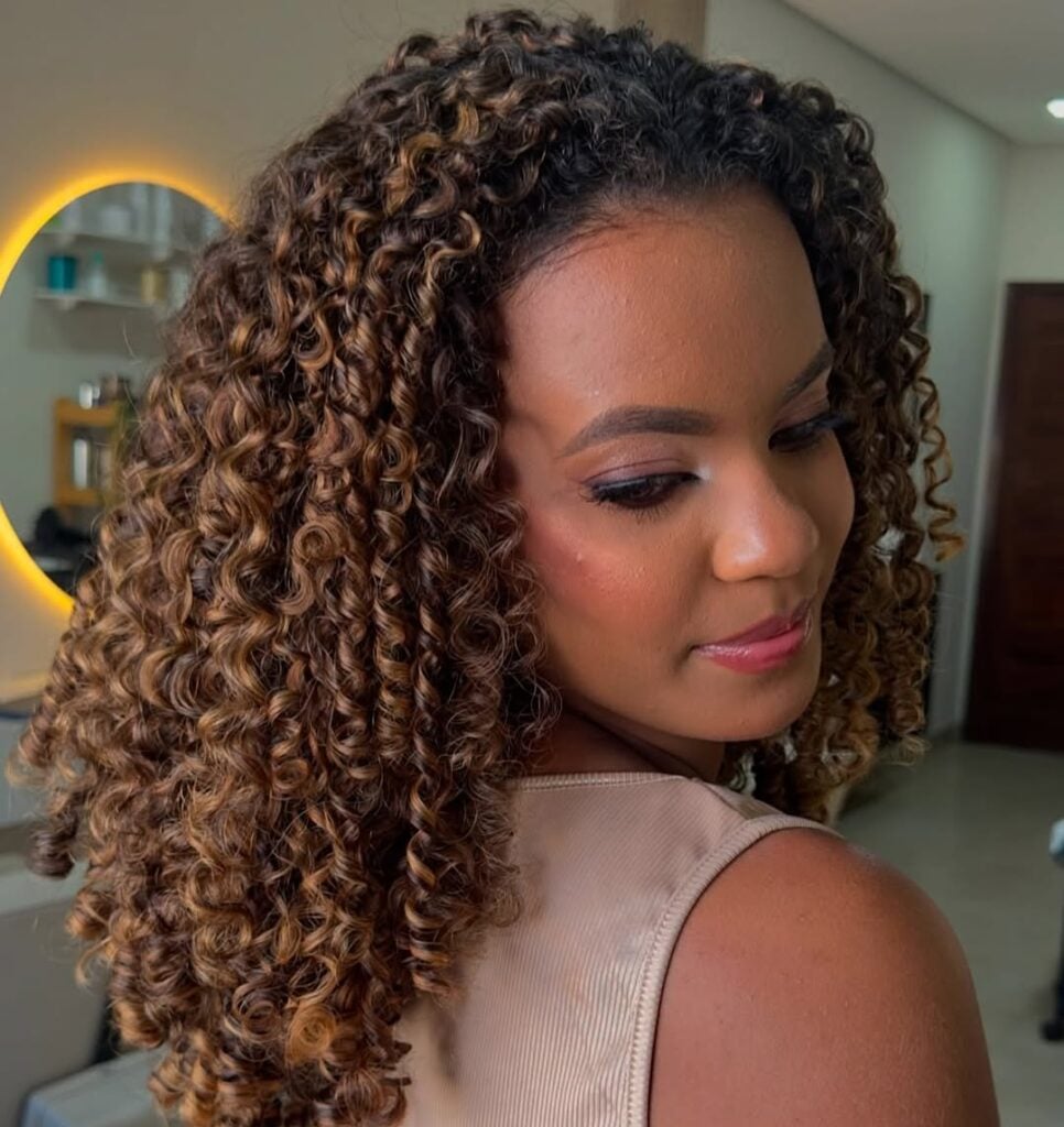 Mulher de pele média, com blusa neutra e cabelo cacheado com luzes