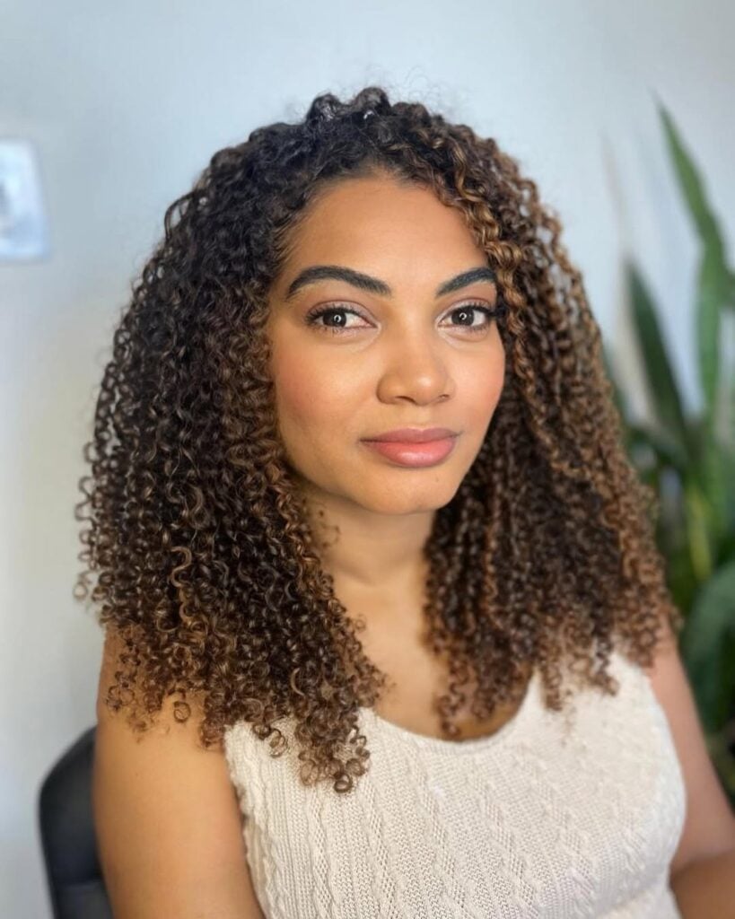 Mulher negra com cabelo longo, crespo e com luzes na técnica morena iluminada na cor caramelo