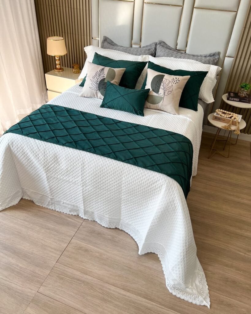 Cama posta com colcha branca, muitas almofadas e manta verde