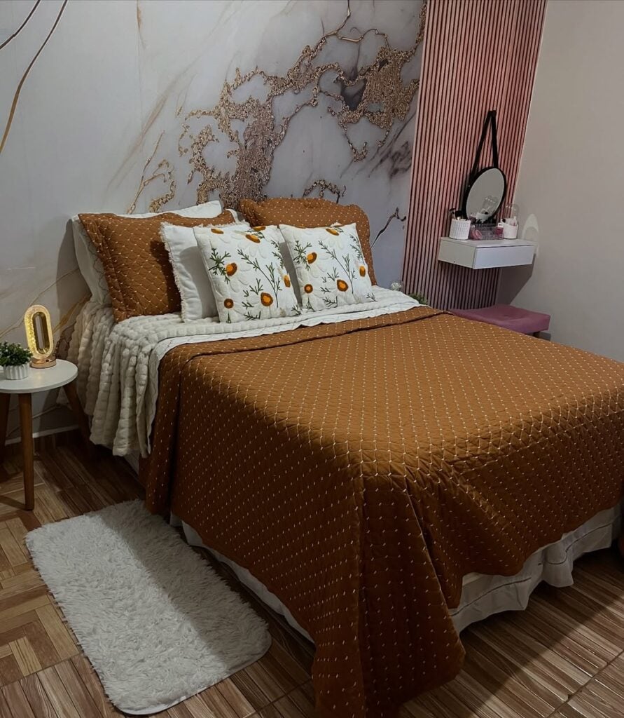 Quarto de casal com papel de parede marmorizado, painel ripado e roupa de cama em tons terrosos