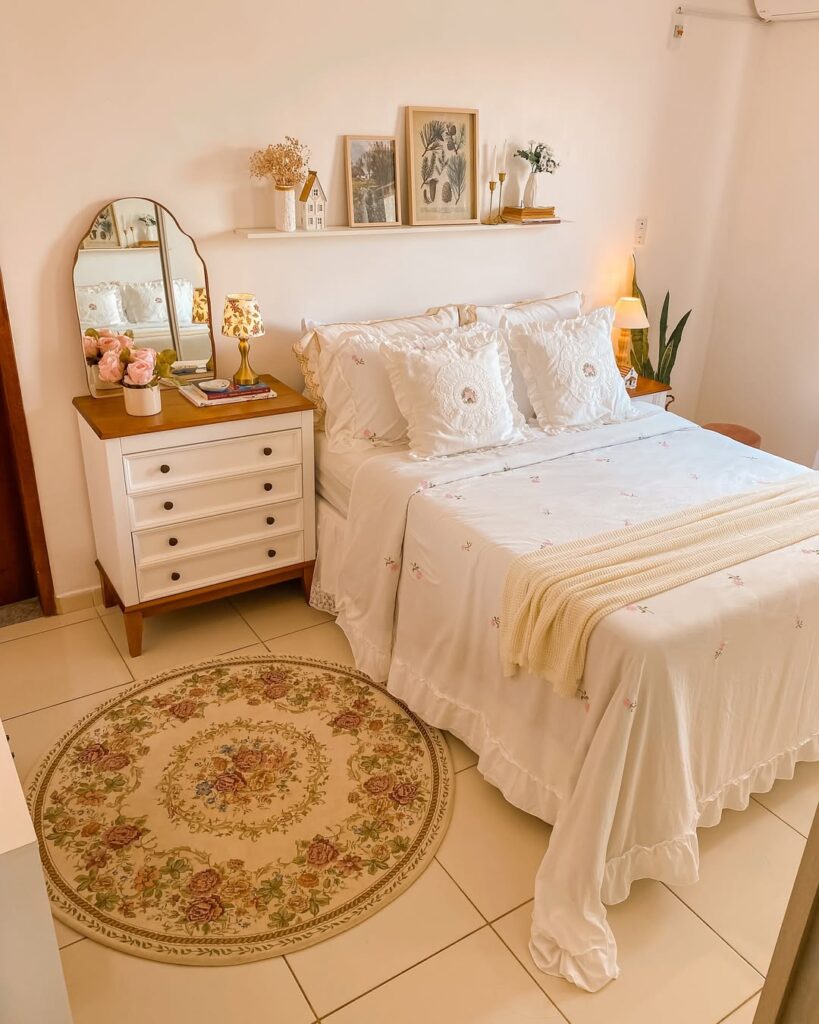 Quarto de casal com cama posta branca, prateleira acima da cabeceira e cômoda com gavetas brancas