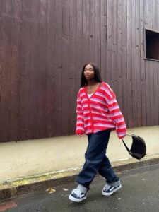 Mulher jovem de pele negra com cardigan listrado, calça jeans e tênis