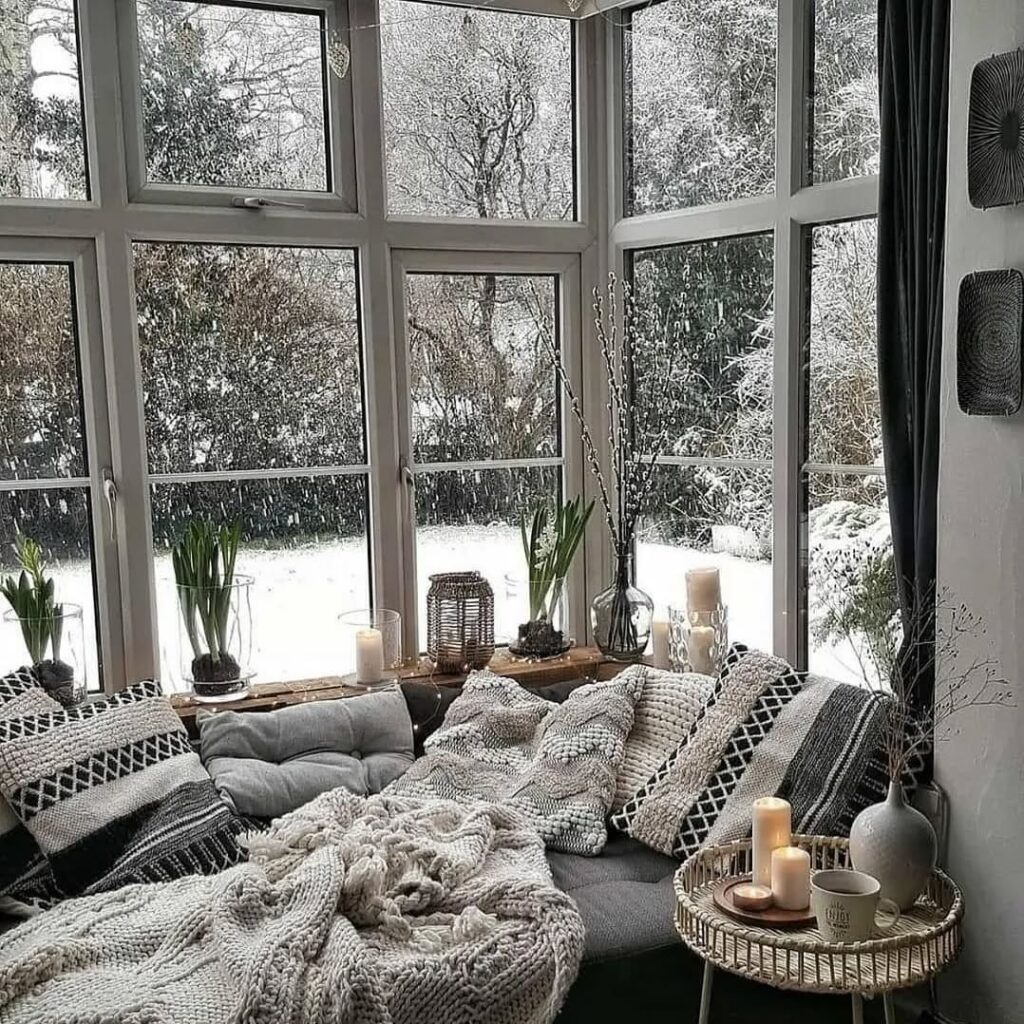 Ambiente com assento e almofadas, mesinha com velas e vaso com flor