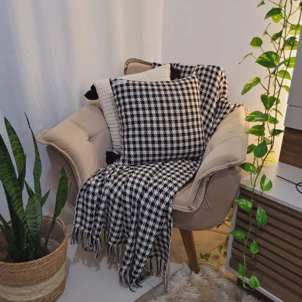 Potrona bege com almofadas bege com preto e xadrez em preto e branco e vaso com plantas
