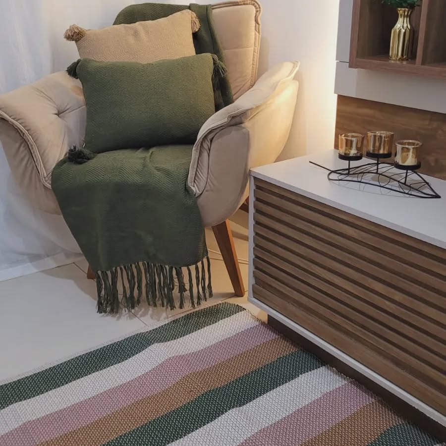 Poltrona bege com pés de madeira, almofadas bege e verde, tapete listrado