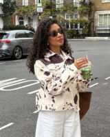 Mulher de pele preta, com cabelo cacheado escuro, calça jeans clara e casaco cow print