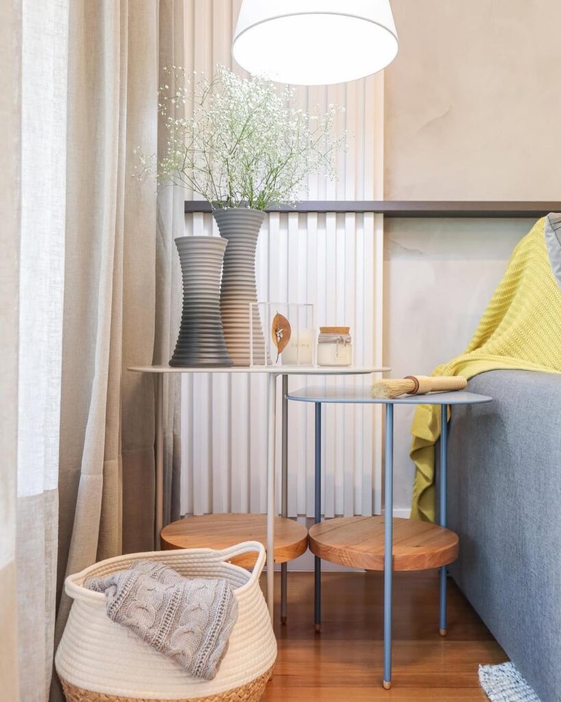 Canto de sala com mesinhas laterais, luminária, vasos com flores e cesto organizador