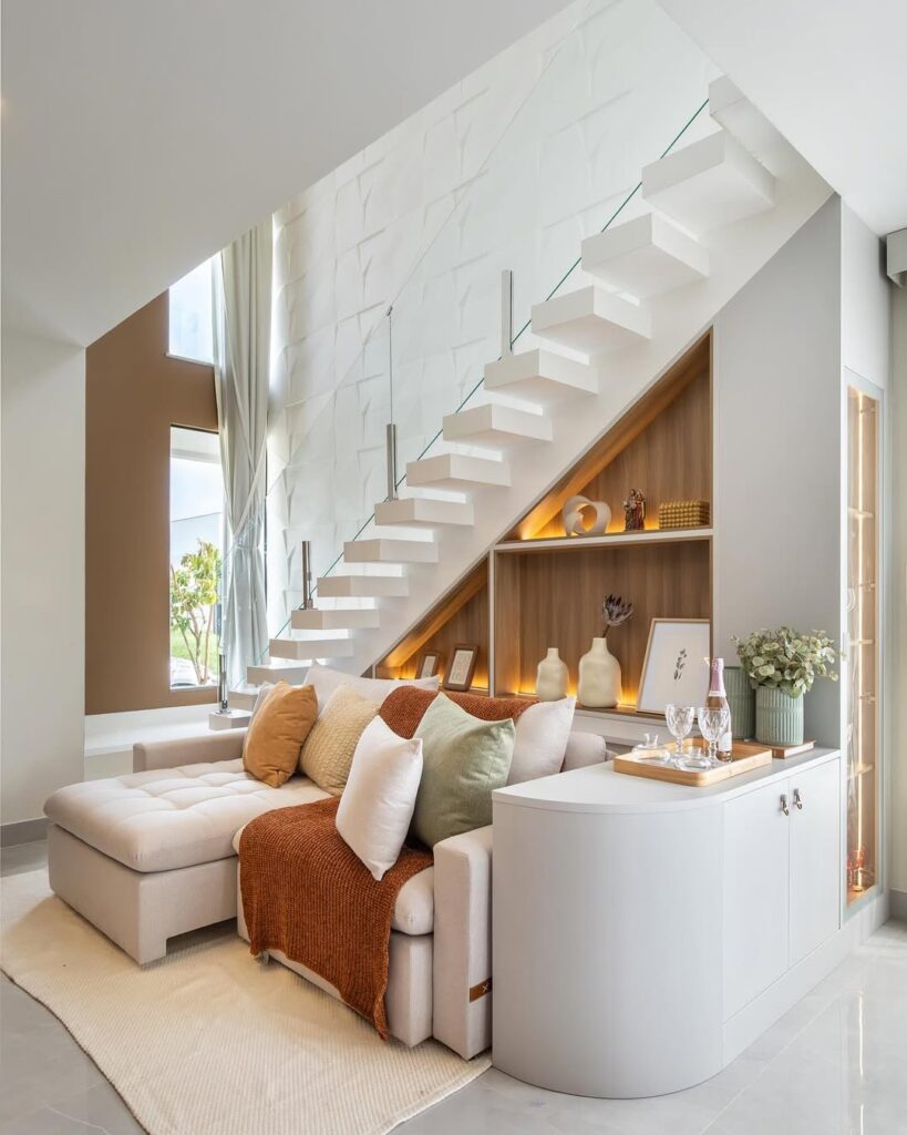 Sala de estar com sofá e balcão orgânico, estante debaixo da escada e manta terracota