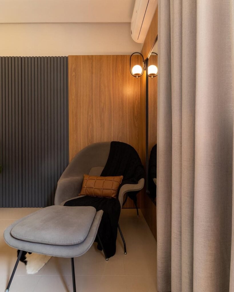 Canto de quarto com poltrona orgânica cinza com peseira e luminária de piso ao lado