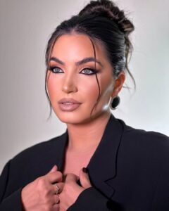 Mulher de pele clara, com blazer preto, cabelo preso e maquiagem com lápis preto