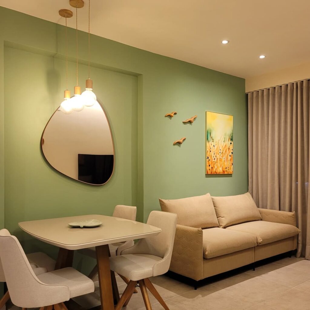 Sala com parede verde-claro, com espelho orgânico, sofá bege e quadro na parede