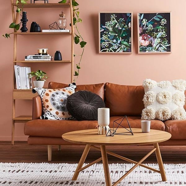 Sala de estar com sofá de couro marrom, parede rosa-queimado com quadros e estante