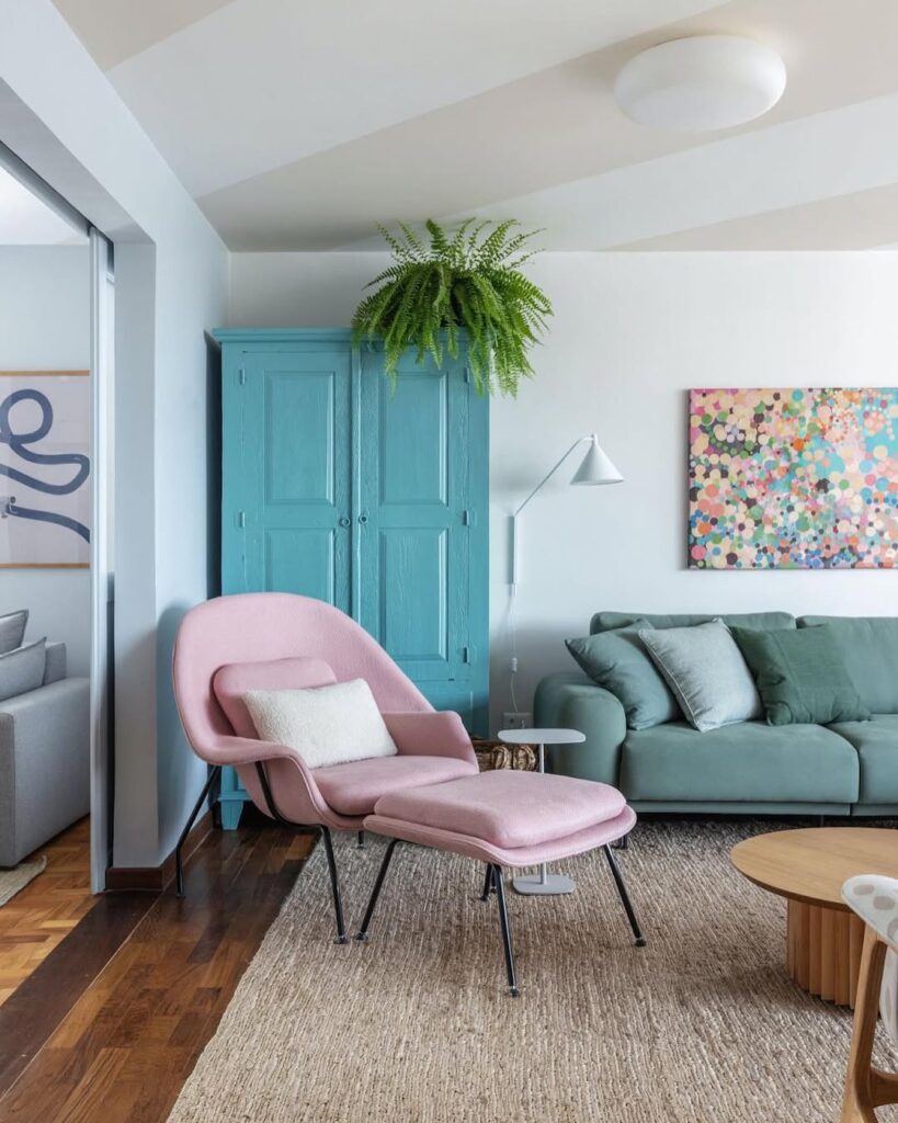 Sala com armário e sofá azul, poltrona rosa e samambaia no teto