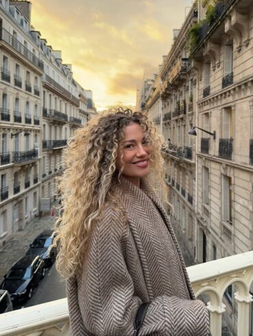 Mulher de pele clara, com casaco e cabelo cacheado loiro