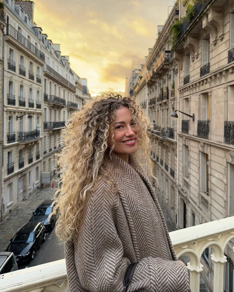 Mulher de pele clara, com casaco e cabelo cacheado loiro