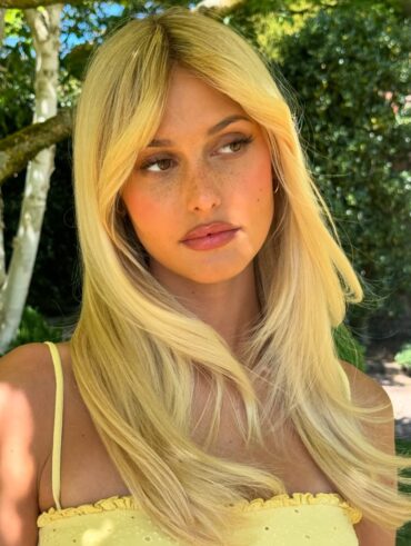 Mulher de pele clara, com blusa de alcinha amarelo-manteiga e cabelo loiro liso