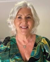 Mulher de pele clara, com blusa estampada, acessório em prata, cabelo grisalho e maquiagem leve