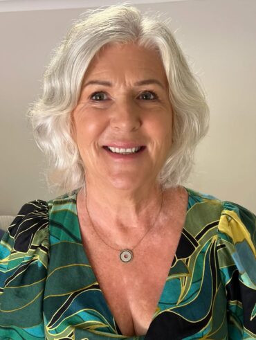 Mulher de pele clara, com blusa estampada, acessório em prata, cabelo grisalho e maquiagem leve