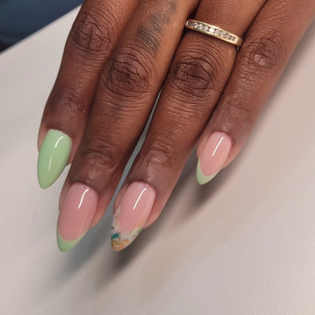 Mão de pele preta, com anel em dourado e unha amendoada verde-claro com francesinha e decoração fluída
