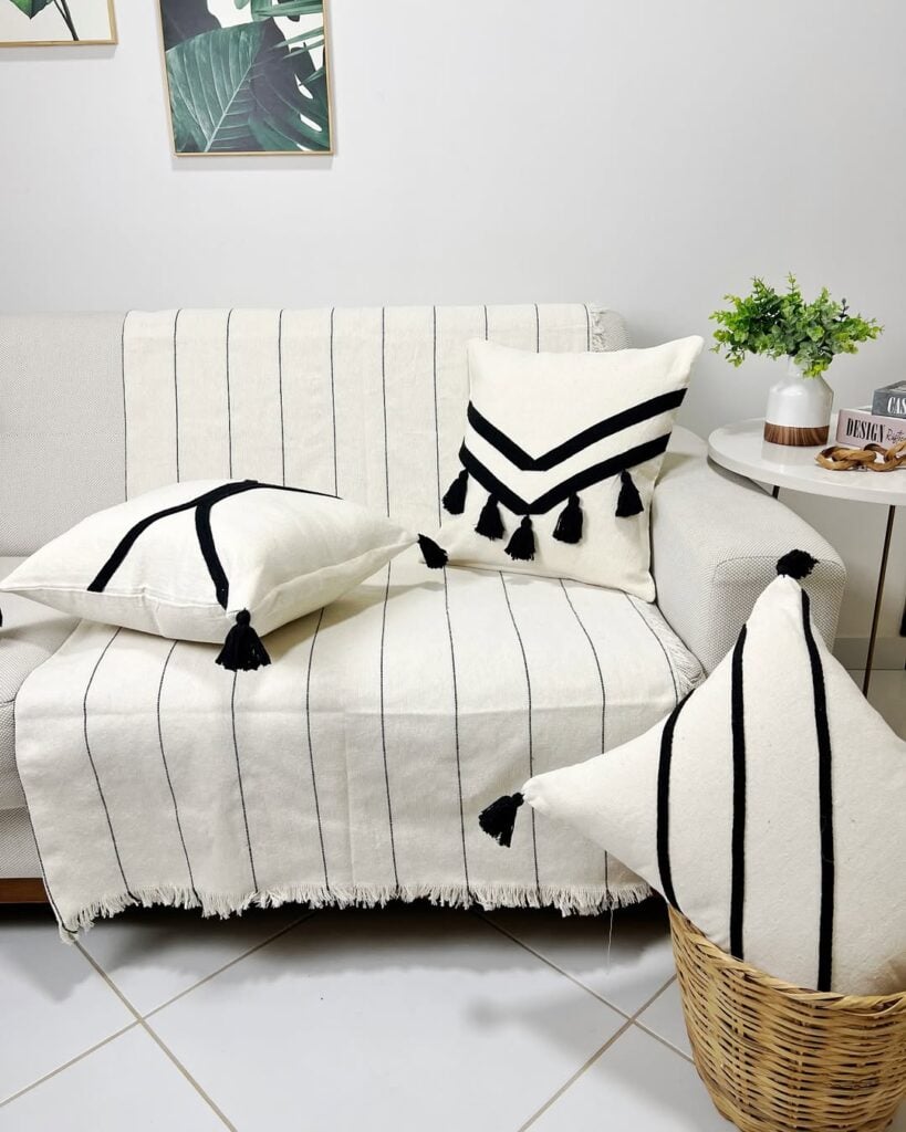 Sala com sofá claro e manta branca com linhas pretas finas e almofadas em branco e preto