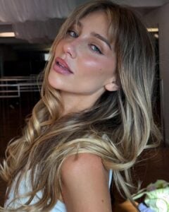 Mulher de pele clara, com regata branca, cabelo liso loiro com franja e maquiagem leve