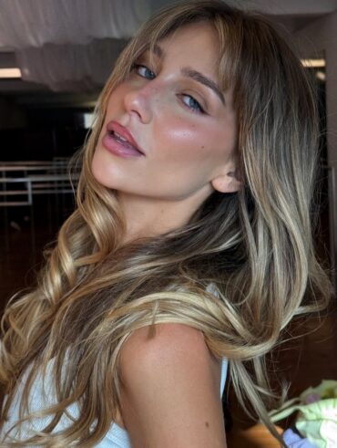 Mulher de pele clara, com regata branca, cabelo liso loiro com franja e maquiagem leve