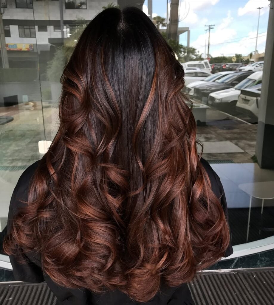 Mulher com cabelo longo, ondulado e com luzes na técnica morena iluminada na cor chocolate
