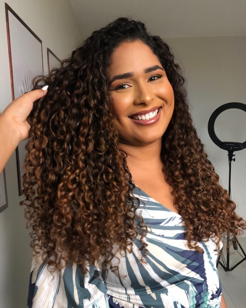 Mulher negra com cabelo longo, cacheado e com luzes na técnica morena iluminada na cor caramelo